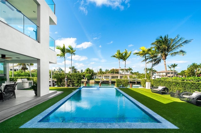 view of pool featuring a yard, ceiling fan, and grilling area