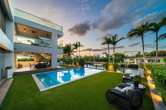 pool at dusk with a lawn, ceiling fan, and a patio area