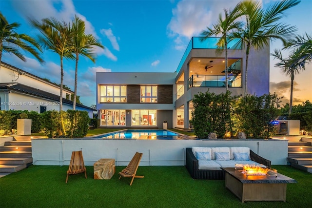 back house at dusk with a fenced in pool, a yard, a balcony, and an outdoor living space with a fire pit