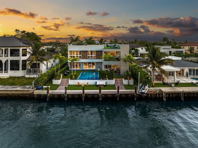 back house at dusk featuring a balcony, a patio area, and a water view