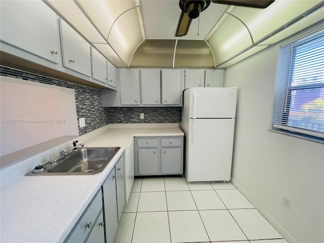 kitchen with white refrigerator, backsplash, light tile floors, sink, and ceiling fan