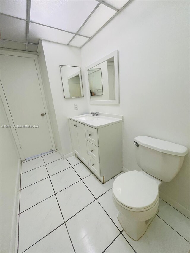 bathroom with vanity with extensive cabinet space, toilet, tile floors, and a drop ceiling