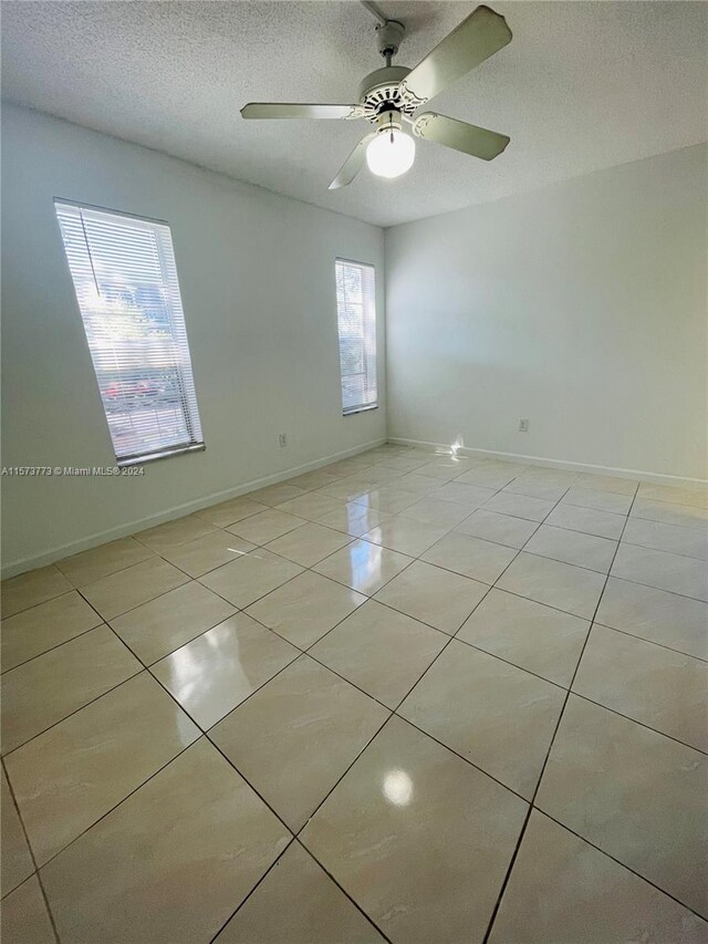 empty room featuring plenty of natural light, a textured ceiling, ceiling fan, and light tile floors