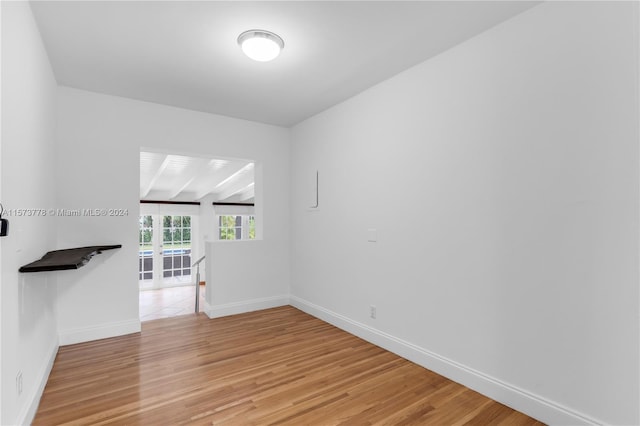 spare room featuring beam ceiling and light hardwood / wood-style floors