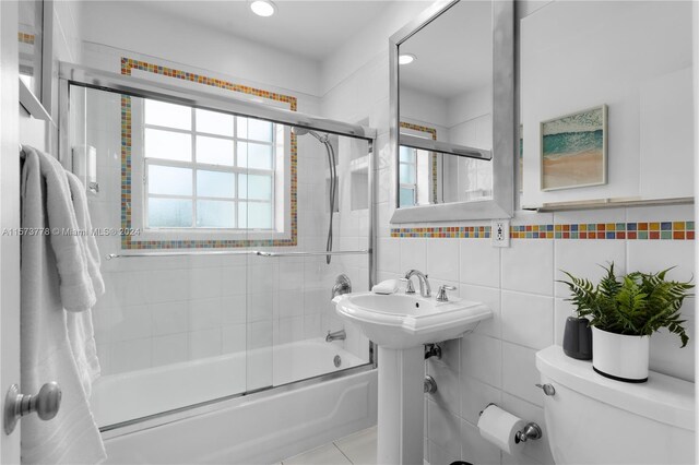 bathroom featuring tile walls, backsplash, toilet, shower / bath combination with glass door, and tile floors