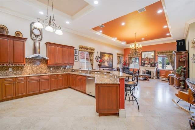 kitchen with pendant lighting, a tray ceiling, wall chimney range hood, and stainless steel dishwasher