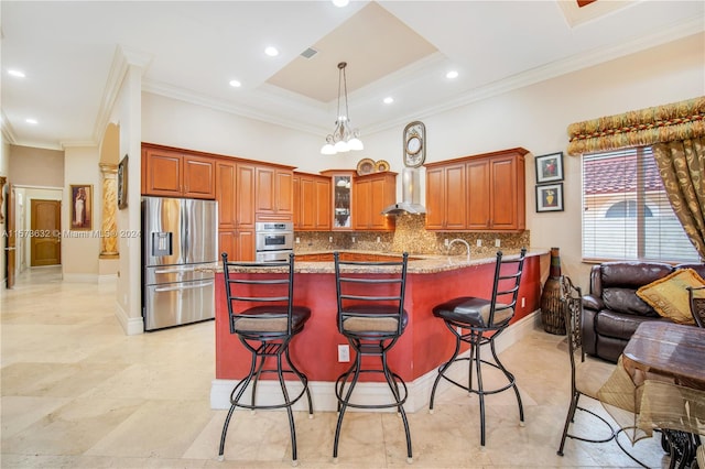 kitchen featuring stainless steel refrigerator with ice dispenser, a tray ceiling, backsplash, wall chimney range hood, and light tile floors