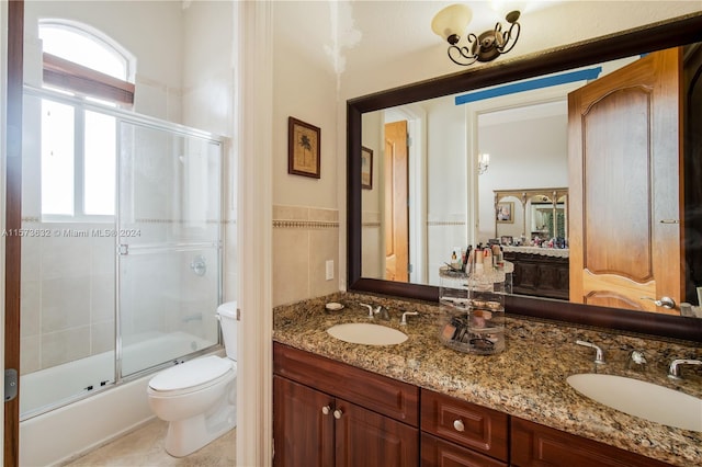 full bathroom with oversized vanity, bath / shower combo with glass door, toilet, tile flooring, and double sink