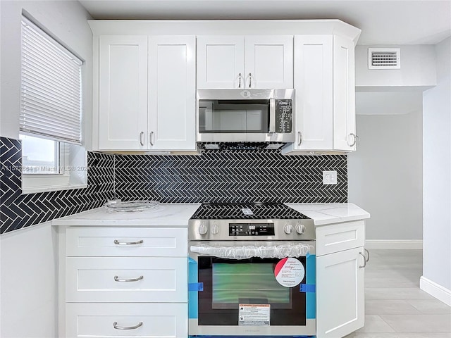 kitchen featuring appliances with stainless steel finishes, white cabinets, backsplash, light hardwood / wood-style flooring, and light stone counters