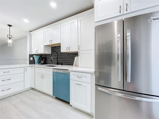 kitchen with stainless steel appliances, white cabinets, decorative light fixtures, light hardwood / wood-style floors, and tasteful backsplash