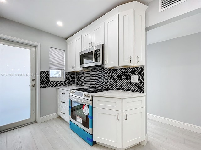 kitchen with tasteful backsplash, light stone countertops, stainless steel appliances, and white cabinetry