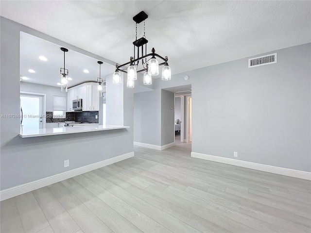 kitchen featuring white cabinetry, light hardwood / wood-style flooring, hanging light fixtures, kitchen peninsula, and backsplash