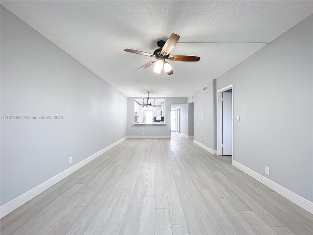 unfurnished room featuring ceiling fan with notable chandelier, a textured ceiling, and light wood-type flooring