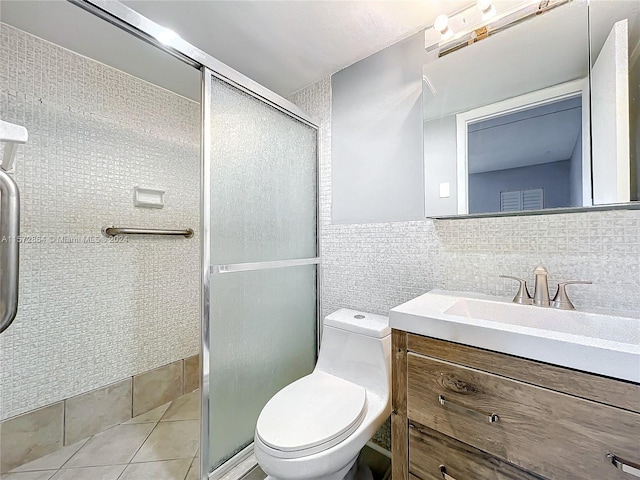 bathroom with tile patterned floors, toilet, tile walls, vanity, and a shower with door