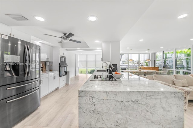 kitchen with a wall of windows, light stone countertops, white cabinets, and appliances with stainless steel finishes