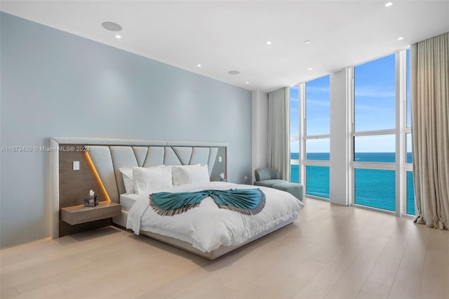 bedroom featuring wood-type flooring, a water view, expansive windows, and access to outside