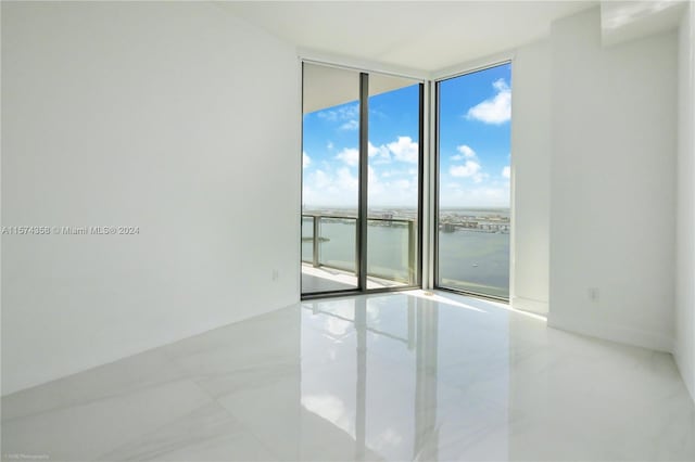 tiled empty room with plenty of natural light, a water view, and a wall of windows