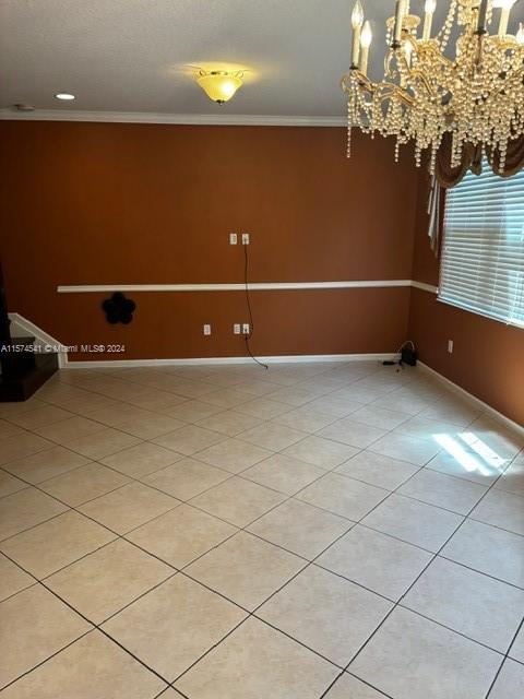 tiled empty room featuring crown molding and a chandelier