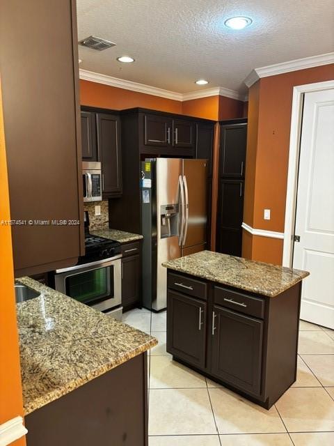 kitchen with appliances with stainless steel finishes, light stone countertops, light tile flooring, and crown molding