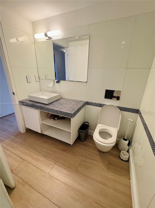 bathroom with hardwood / wood-style flooring, vanity, toilet, and tile walls