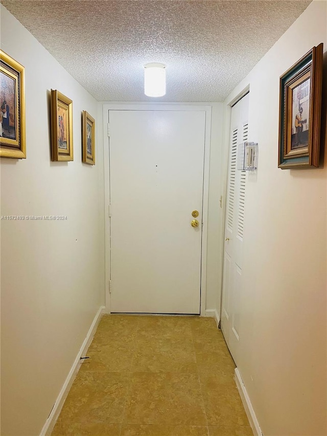 hall with a textured ceiling and light tile patterned floors