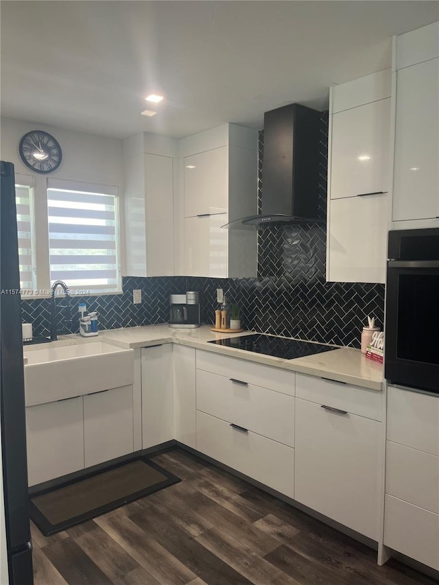 kitchen featuring wall chimney range hood, tasteful backsplash, dark hardwood / wood-style flooring, white cabinetry, and black appliances