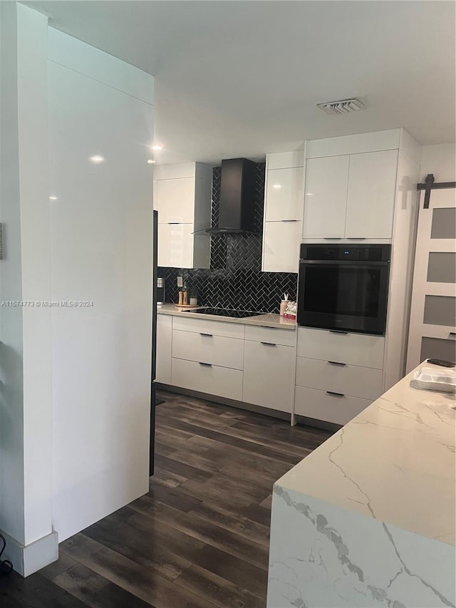 kitchen with black appliances, a barn door, dark hardwood / wood-style flooring, wall chimney exhaust hood, and white cabinets