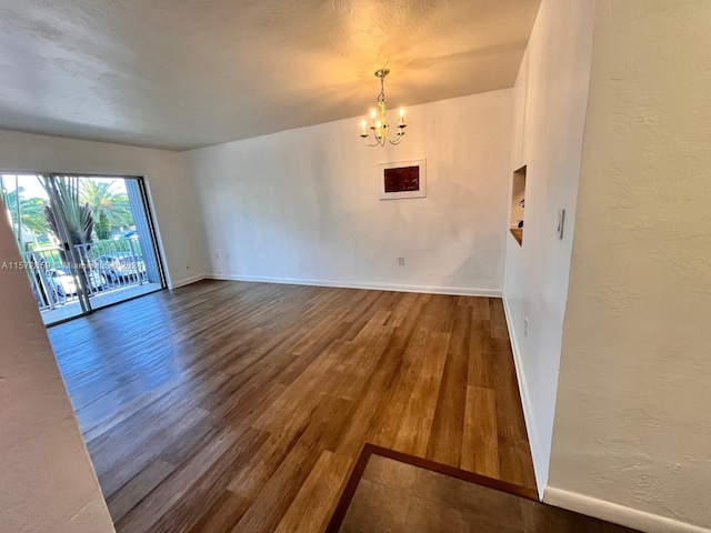 unfurnished room with a notable chandelier and dark wood-type flooring