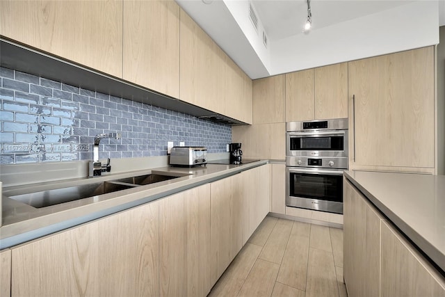 kitchen with a sink, double oven, light brown cabinets, and light countertops