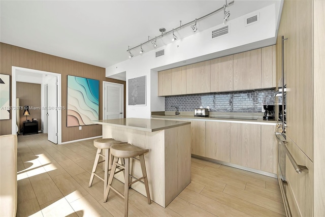 kitchen with light brown cabinets, visible vents, a breakfast bar, and a center island