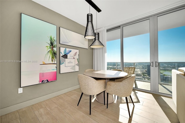 dining area featuring a wall of windows, light wood-type flooring, and baseboards