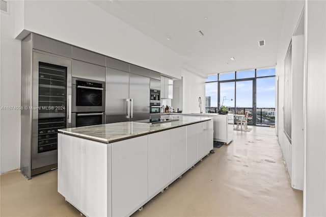 kitchen featuring expansive windows, appliances with stainless steel finishes, light stone counters, sink, and a center island