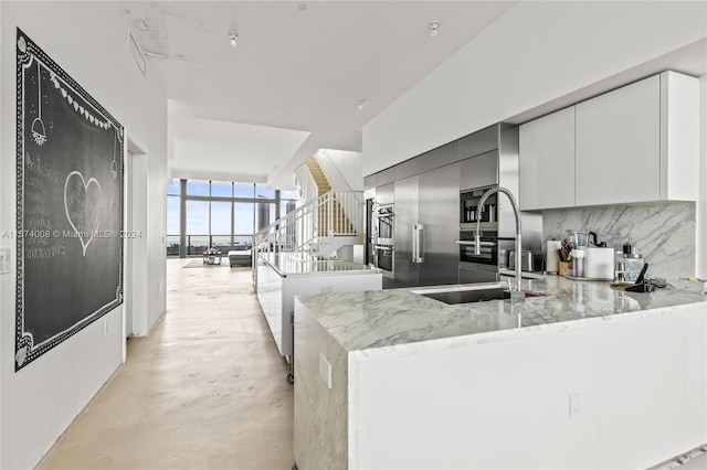 kitchen with tasteful backsplash, kitchen peninsula, sink, and light stone counters