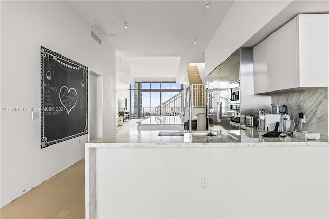 kitchen with tasteful backsplash, light stone countertops, sink, and kitchen peninsula