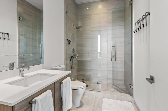 bathroom featuring a shower with shower door, vanity with extensive cabinet space, toilet, and tile flooring