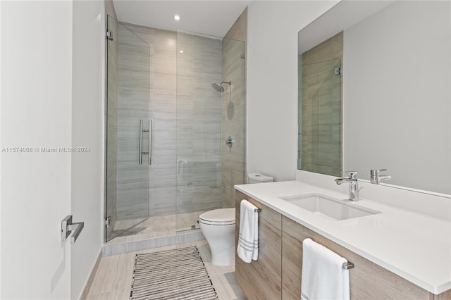 bathroom with vanity with extensive cabinet space, a shower with shower door, toilet, and tile flooring