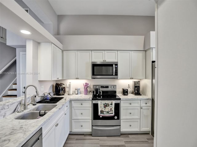 kitchen with white cabinets, appliances with stainless steel finishes, sink, and light stone countertops