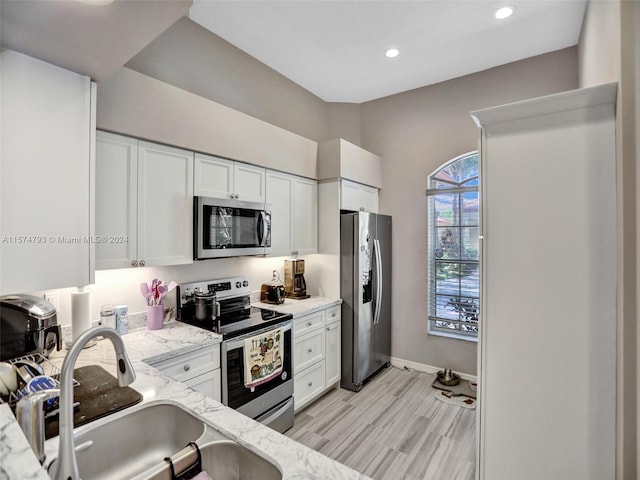 kitchen with white cabinetry, light hardwood / wood-style floors, appliances with stainless steel finishes, light stone counters, and sink