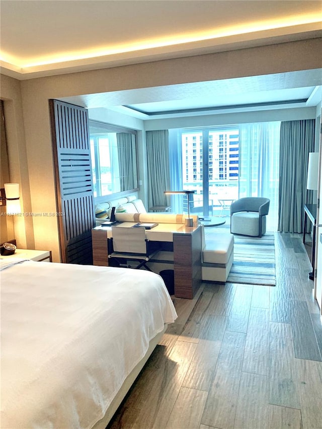 bedroom featuring wood-type flooring, a raised ceiling, and multiple windows