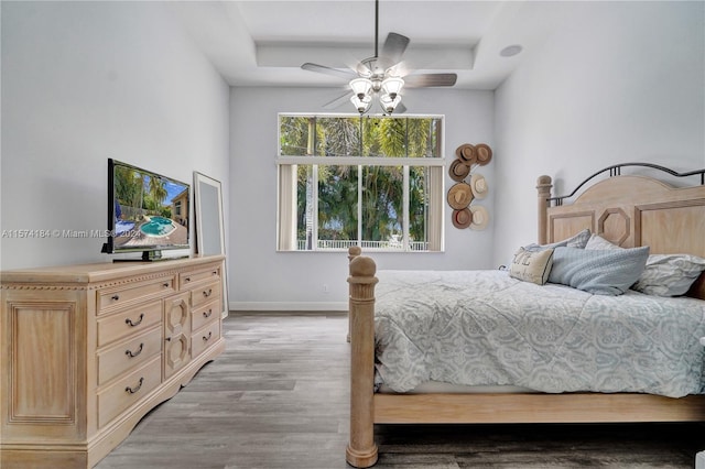 bedroom featuring ceiling fan, a raised ceiling, and light hardwood / wood-style floors