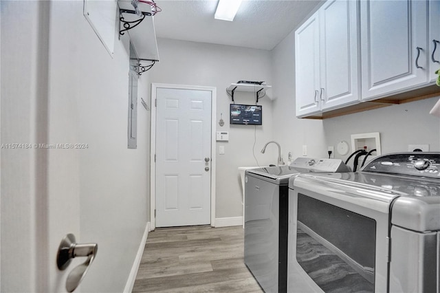 laundry room with a textured ceiling, light hardwood / wood-style floors, washer and dryer, and cabinets