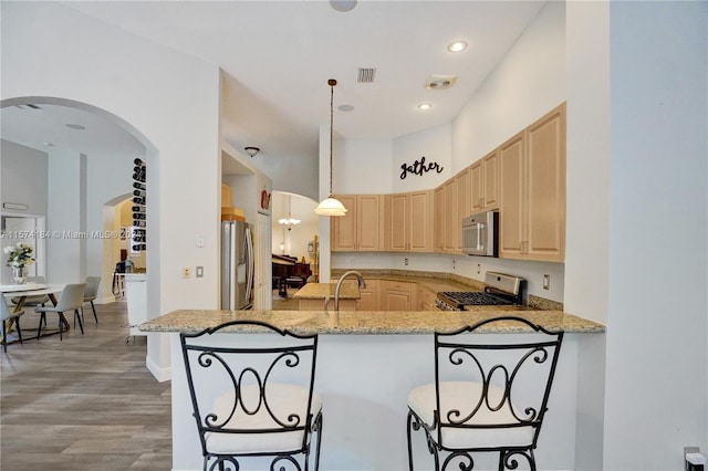 kitchen with light brown cabinets, kitchen peninsula, decorative light fixtures, light hardwood / wood-style flooring, and stainless steel appliances