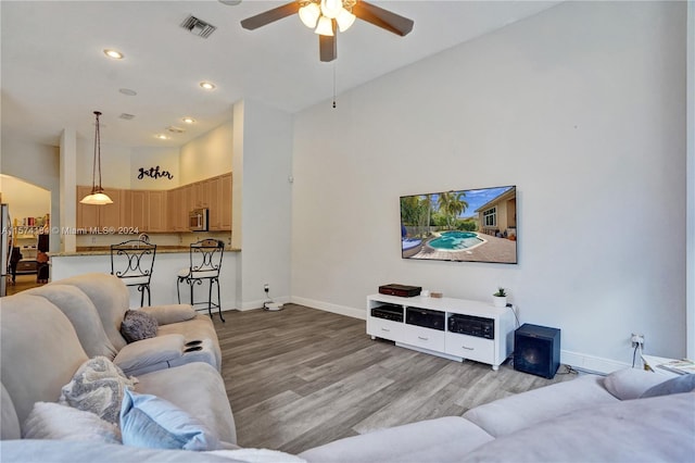 living room with light wood-type flooring, ceiling fan, and a high ceiling