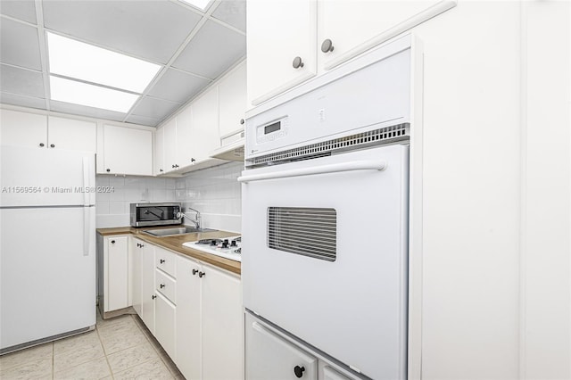 kitchen with a drop ceiling, white appliances, tasteful backsplash, white cabinets, and light tile floors