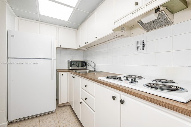 kitchen with white appliances, light tile flooring, tasteful backsplash, white cabinets, and sink