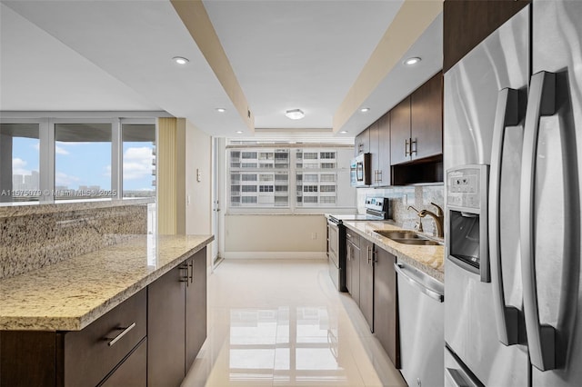 kitchen with recessed lighting, a raised ceiling, appliances with stainless steel finishes, a sink, and dark brown cabinets