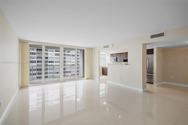 empty room featuring expansive windows, visible vents, and baseboards