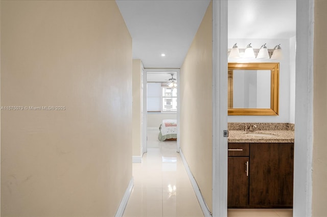 hall featuring light tile patterned flooring, a sink, and baseboards