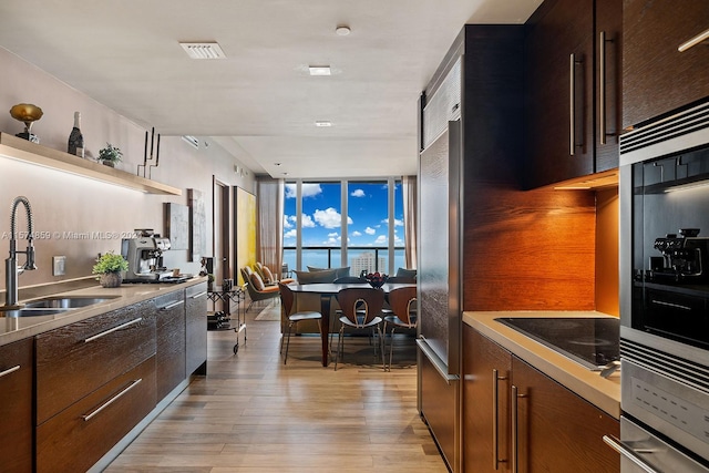 kitchen featuring expansive windows, black electric stovetop, oven, sink, and light wood-type flooring