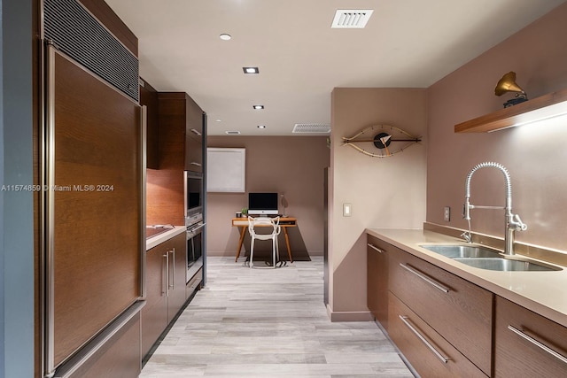 kitchen featuring sink, light wood-type flooring, paneled built in refrigerator, and oven